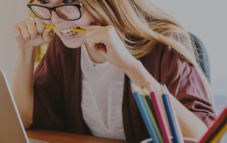 Girl biting on pencil with anxious look on her face while looking at her laptop