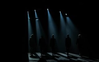 dark stage with actors on it to help show the idea a Play That Started in the Dark